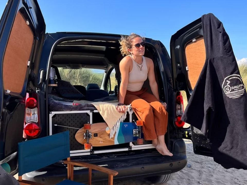 Woman sitting in the back of a camper van with a skateboard.