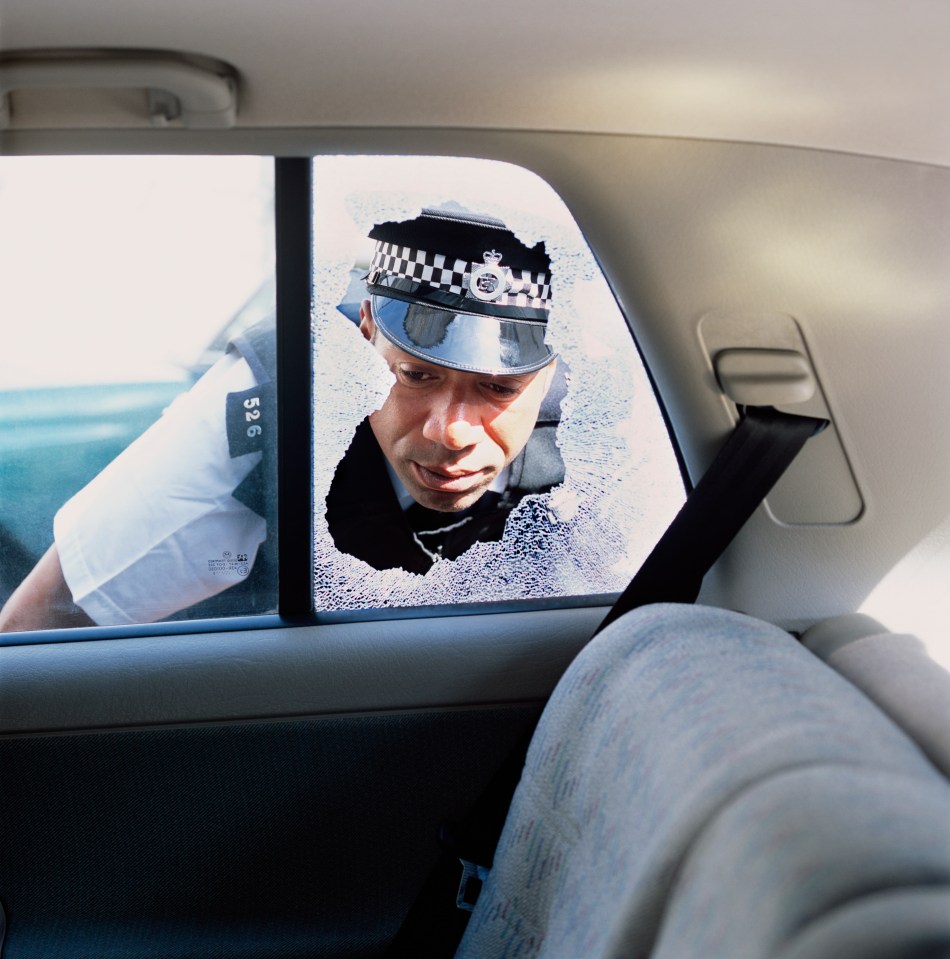 Police officer examining the interior of a car with a broken rear window.