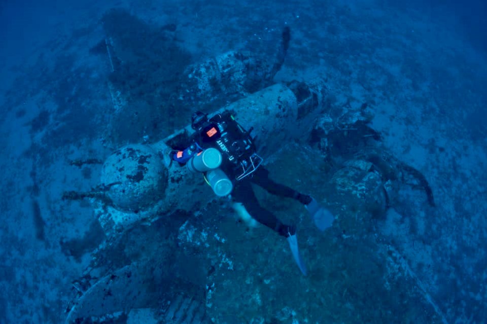 Diver exploring a WWII plane wreck underwater.