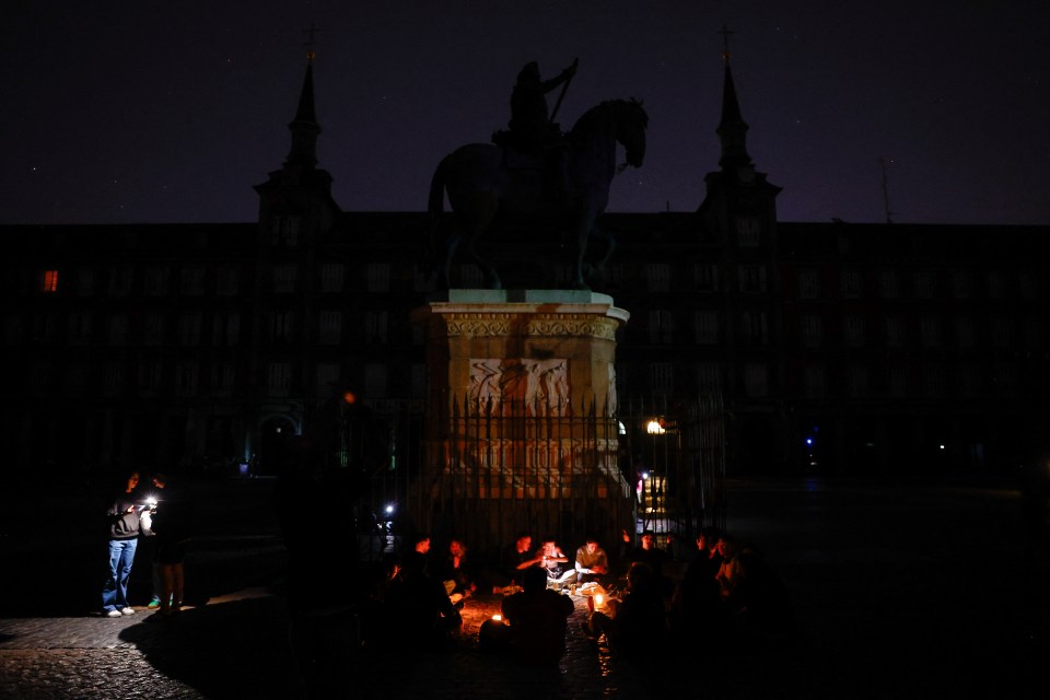People using phone flashlights in a dark plaza during a power outage.