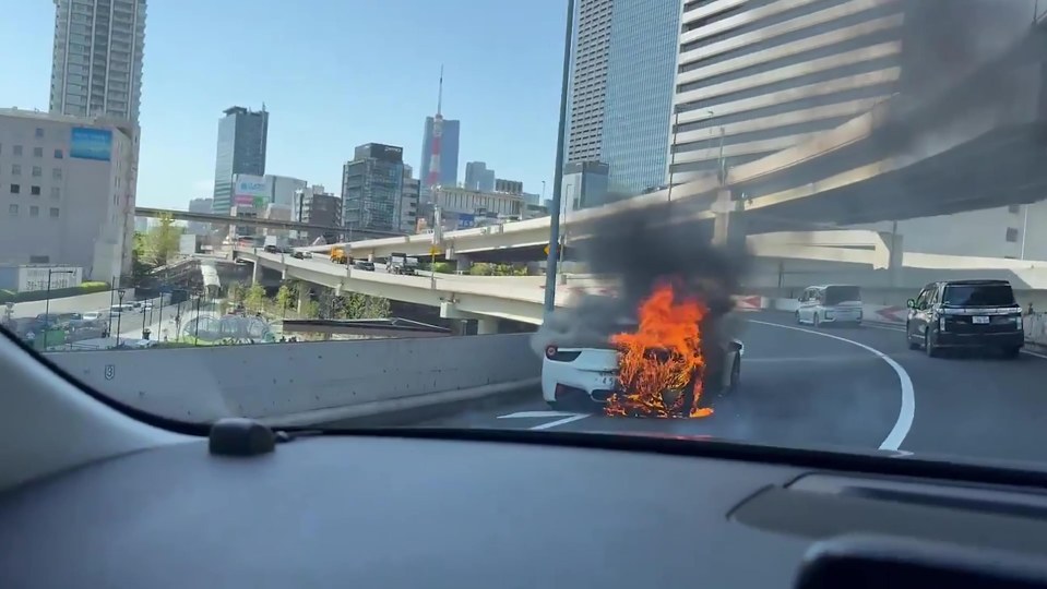 A white Ferrari engulfed in flames on a city highway.