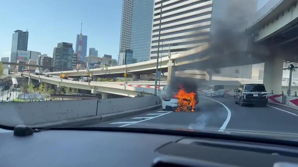 A Ferrari on fire on a city highway.