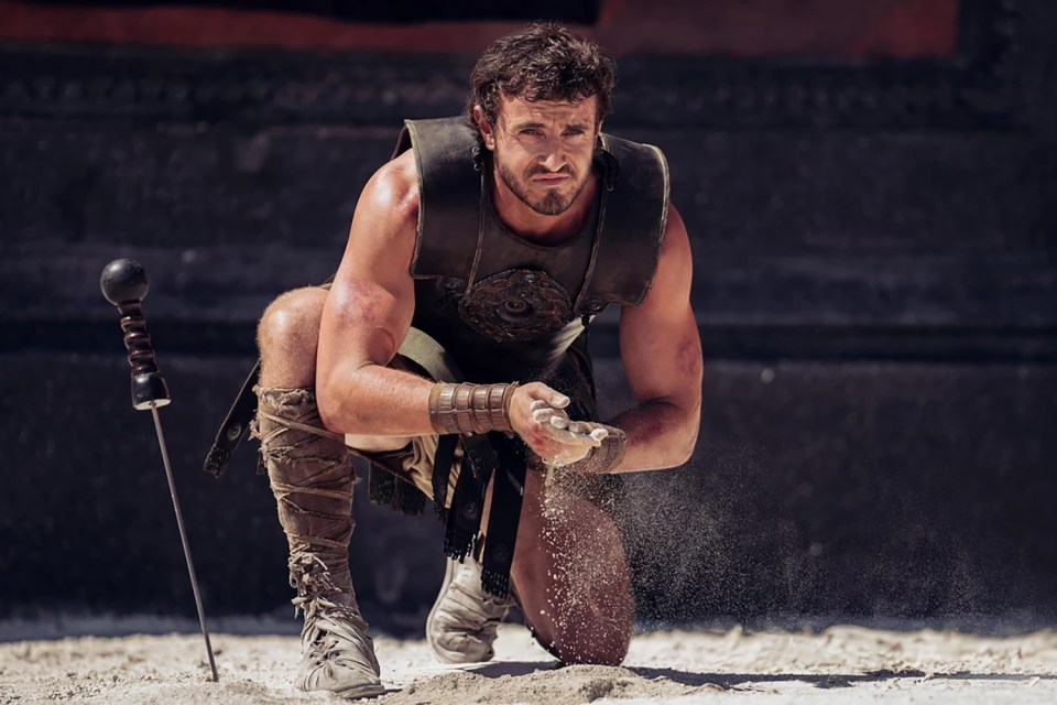 A gladiator kneeling and letting sand fall through his hands.