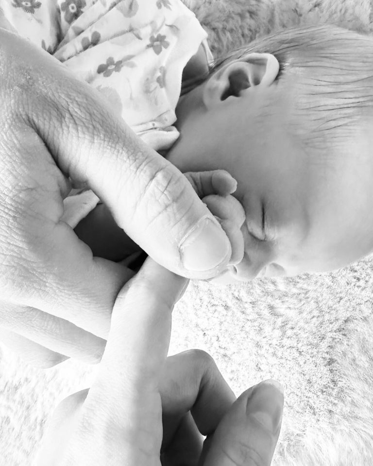 Black and white photo of adult hands holding a newborn baby's hand.