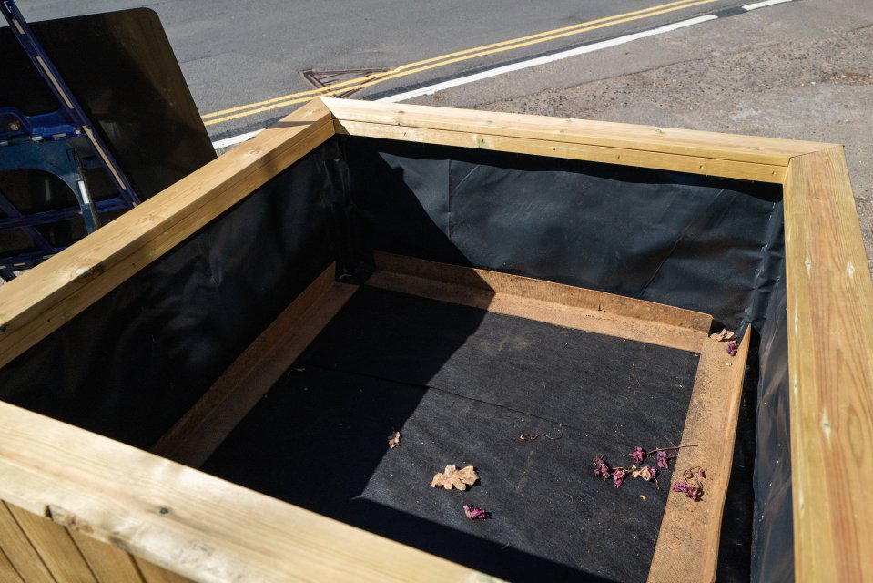 Empty wooden planter box lined with black fabric.