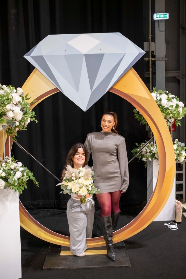 Two women at a wedding show posing with a large ring prop.