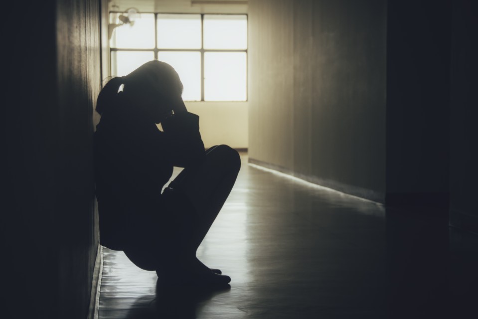 Silhouette of a woman sitting alone, head in hands.