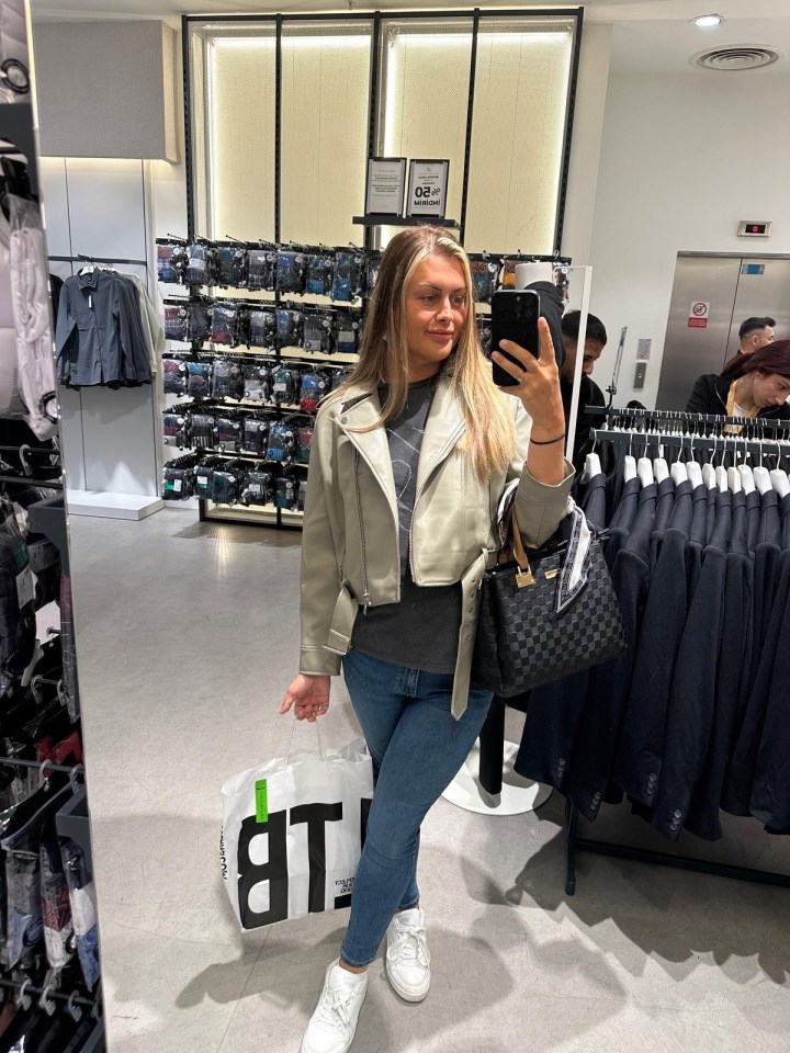 Woman in a beige jacket taking a selfie in a clothing store.