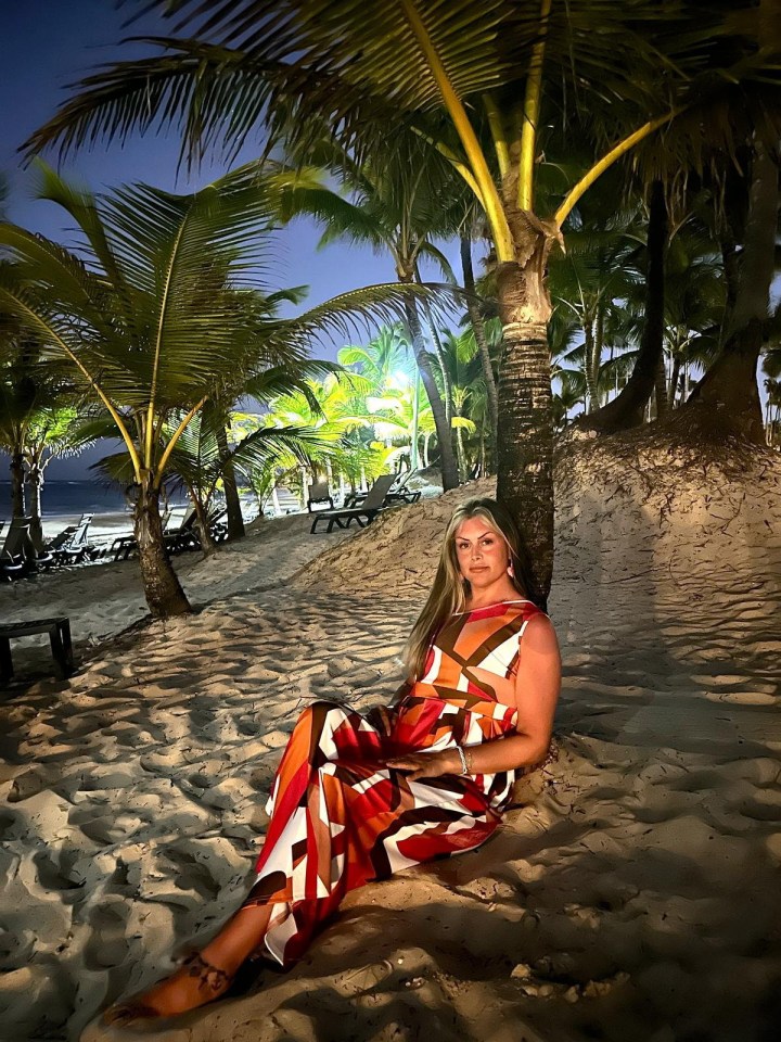 Woman in geometric print dress sitting on a beach at night under palm trees.