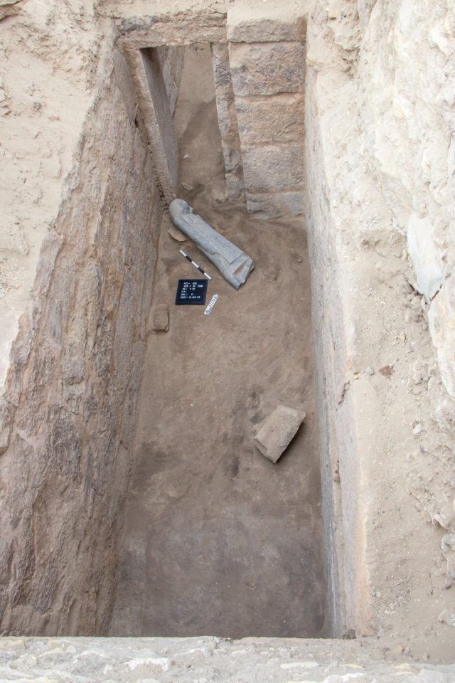 Overhead view of an archaeological excavation site showing a stone statue fragment and other artifacts in the Saqqara necropolis.