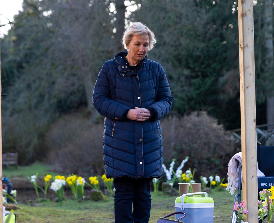 A woman in a dark blue coat stands outdoors, looking down.