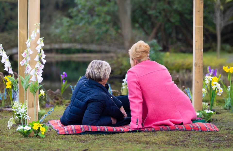 Two women sitting on a blanket outdoors, facing away from the camera.