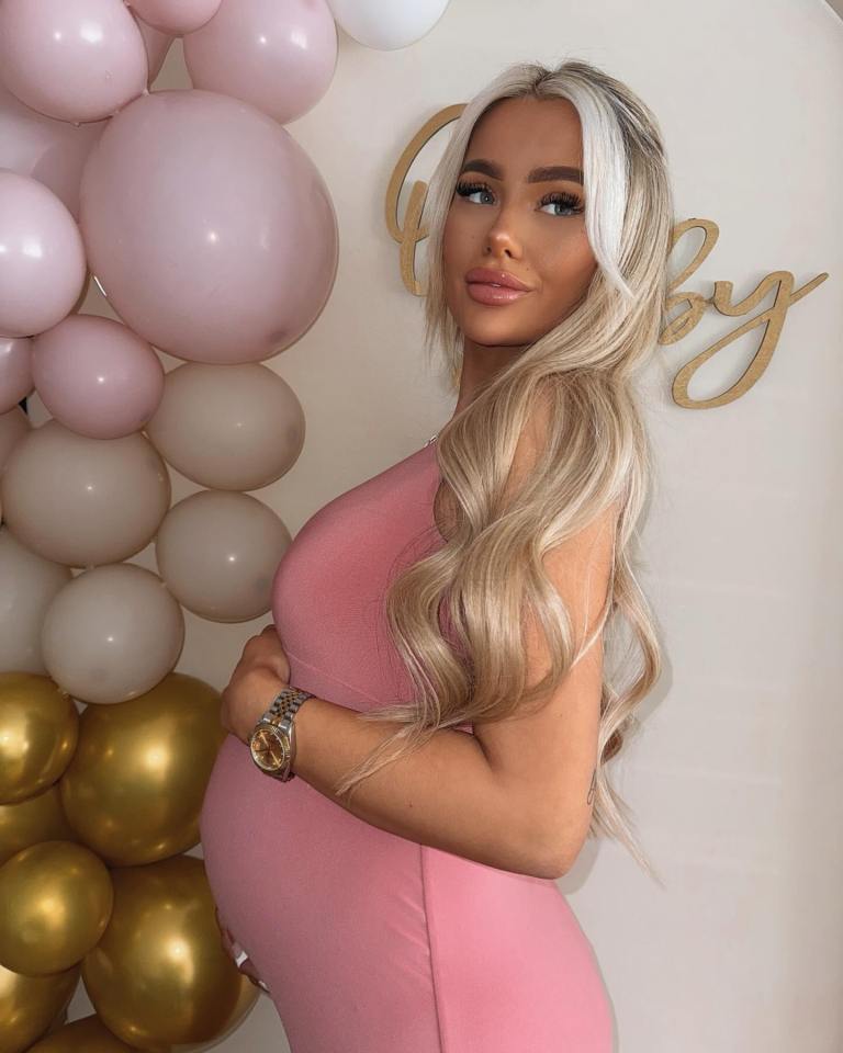 Pregnant woman in pink dress in front of balloons and "baby" sign.