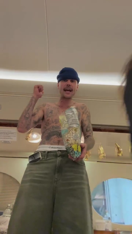 Justin Bieber shirtless on a private jet, holding a bag of popcorn.