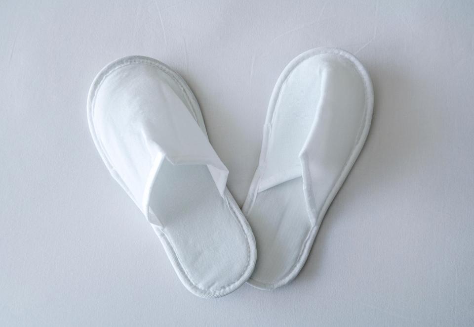 Pair of white disposable hotel slippers on a white bedsheet.