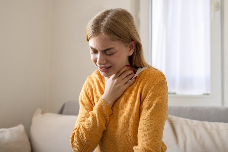 Woman holding her throat, appearing unwell.