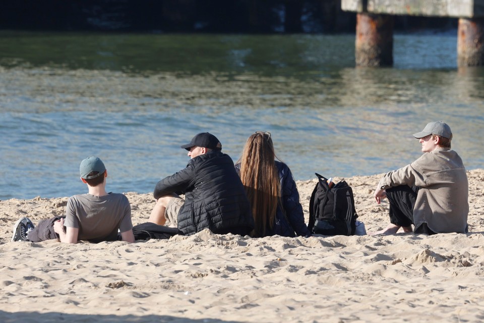 Four people sitting on a sandy beach near the water.