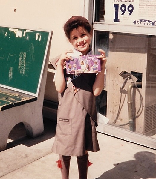 Young Meghan Markle in Girl Scout uniform selling cookies.