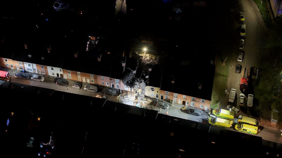 Aerial view of a house explosion at night with emergency services responding.