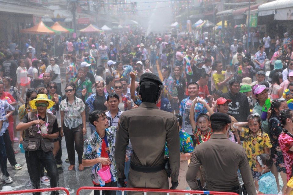 A police officer standing in the midst of a large crowd participating in a water festival.