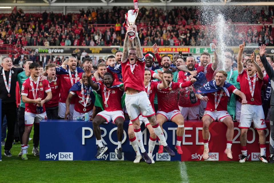 Wrexham AFC players celebrating a victory and lifting a trophy.