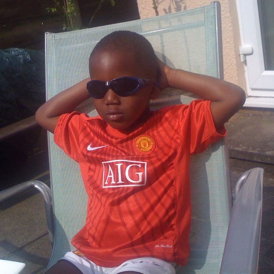 Young boy wearing sunglasses and a Manchester United jersey, relaxing in a lawn chair.