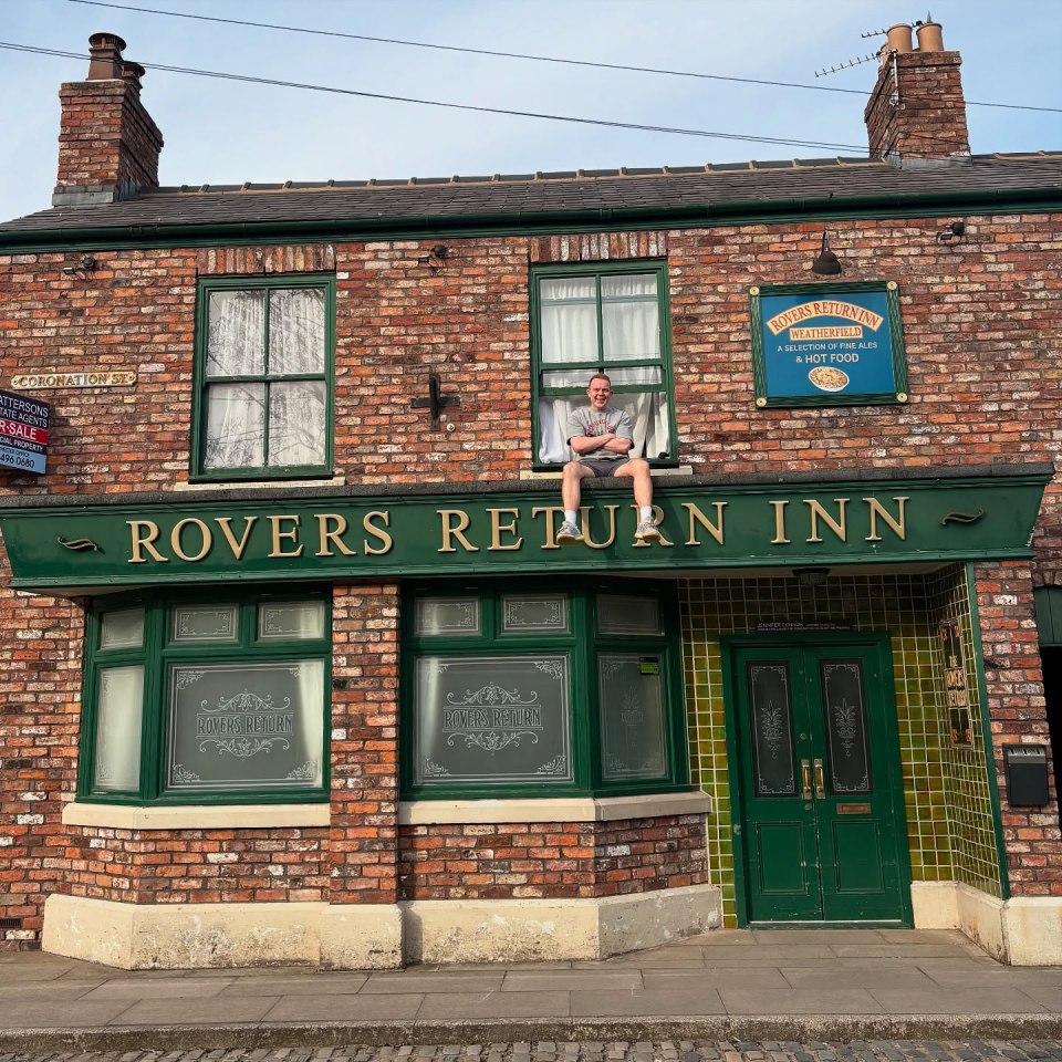 Man sitting on the Rovers Return Inn sign.