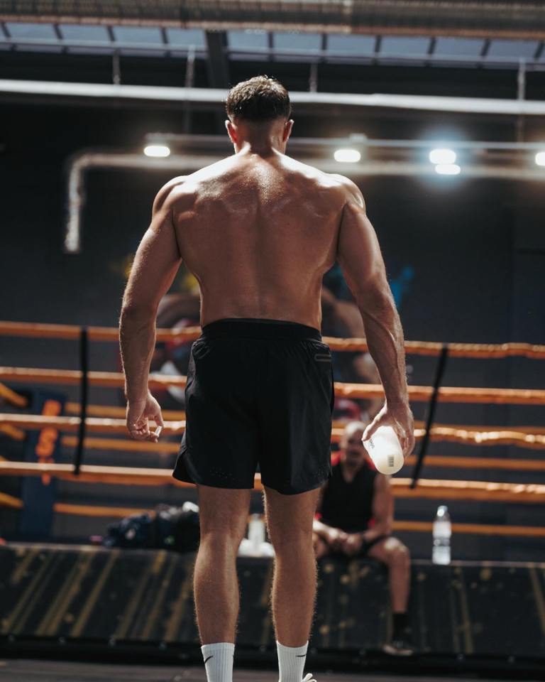 Muscular man's back, holding a water bottle in a boxing gym.