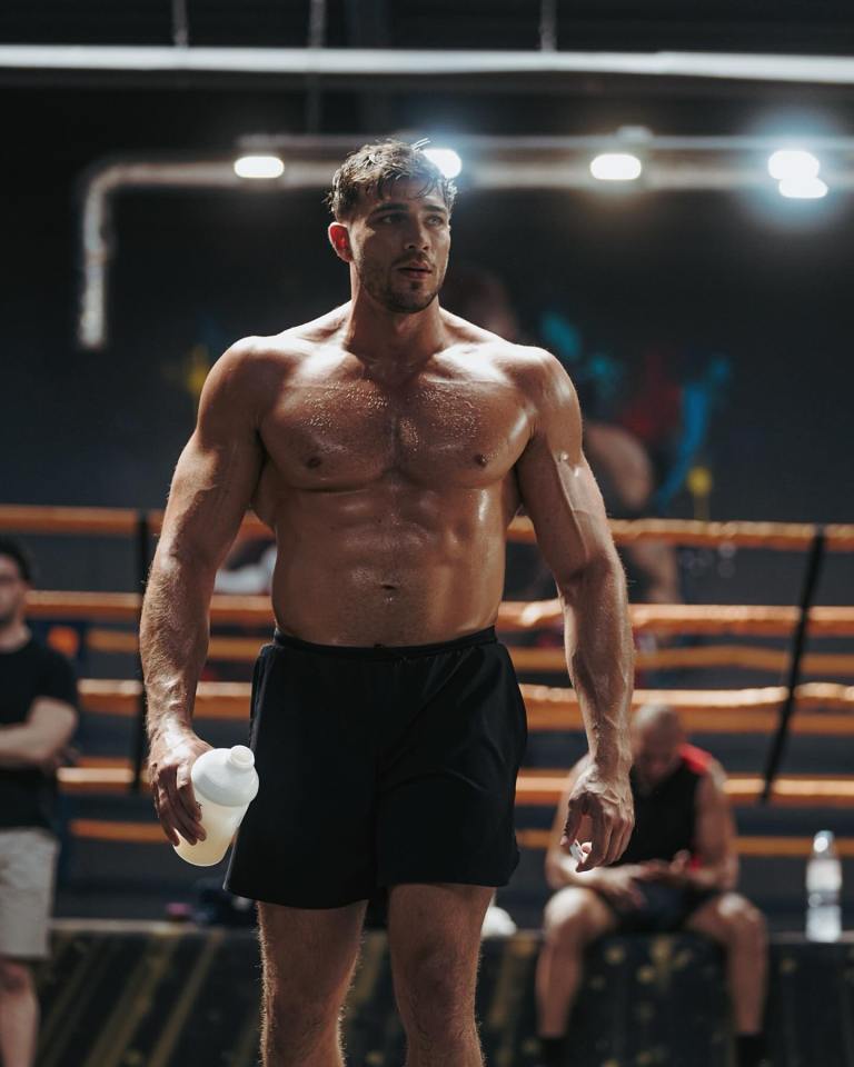 Sweaty muscular man holding a water bottle in a boxing gym.