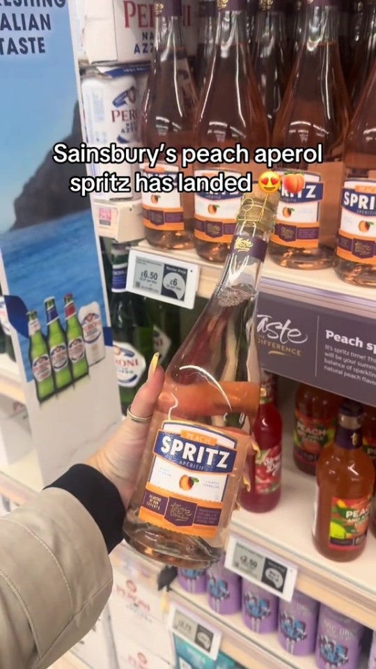 A hand holding a bottle of Sainsbury's peach aperol spritz in a store.