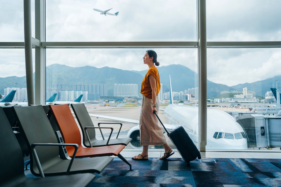Woman pulling suitcase in airport terminal.