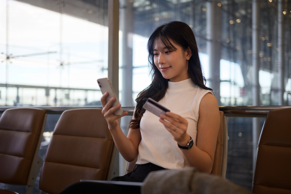 Young woman using smartphone and credit card to make an online purchase at the airport.