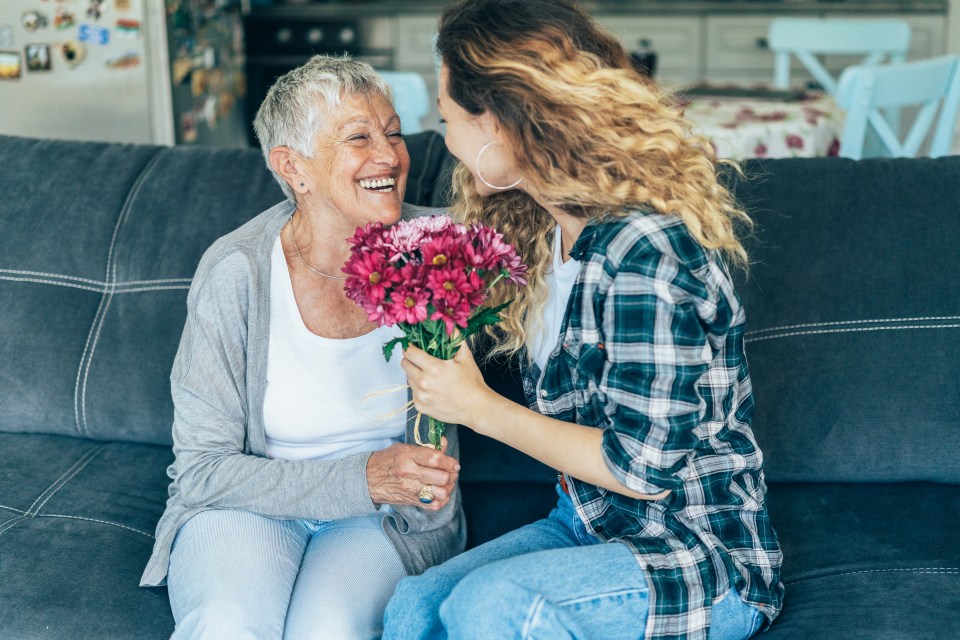 A young woman gives her mother a bouquet of flowers.