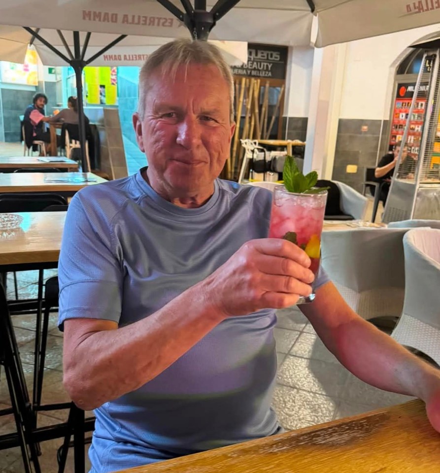 A man holds a cocktail at an outdoor cafe.