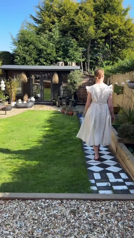 Woman walking on a black and white patio path in a garden.