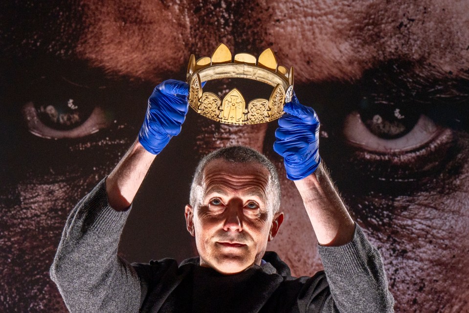 A person in blue gloves holds up a replica crown from the 2015 film adaptation of Macbeth.
