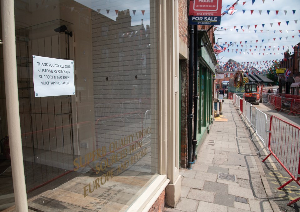 Roadworks and barriers dominate a small town street, with a closed shop displaying a thank you note.