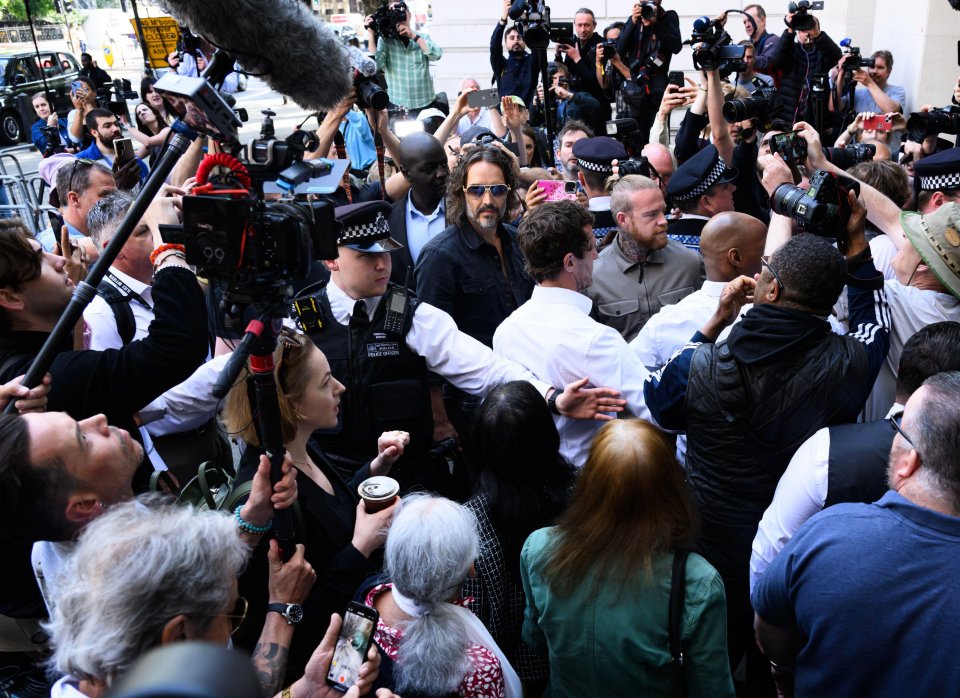 Russell Brand leaving Westminster Magistrates Court, surrounded by police and press.