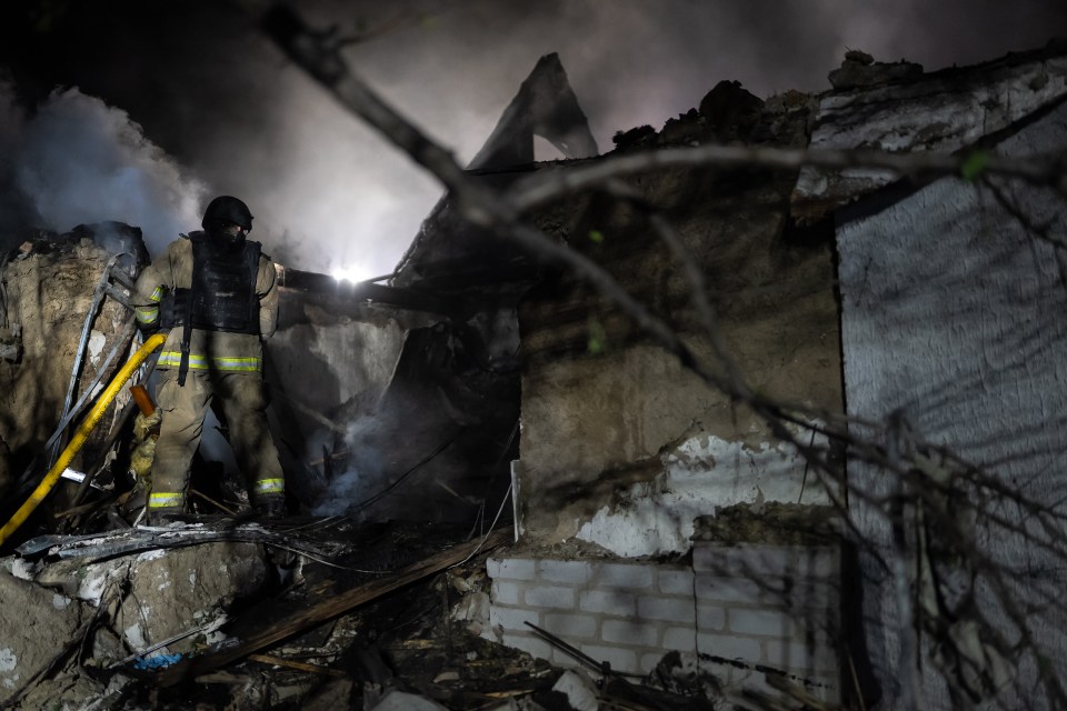 Firefighter at night amidst the rubble of a bombed building.