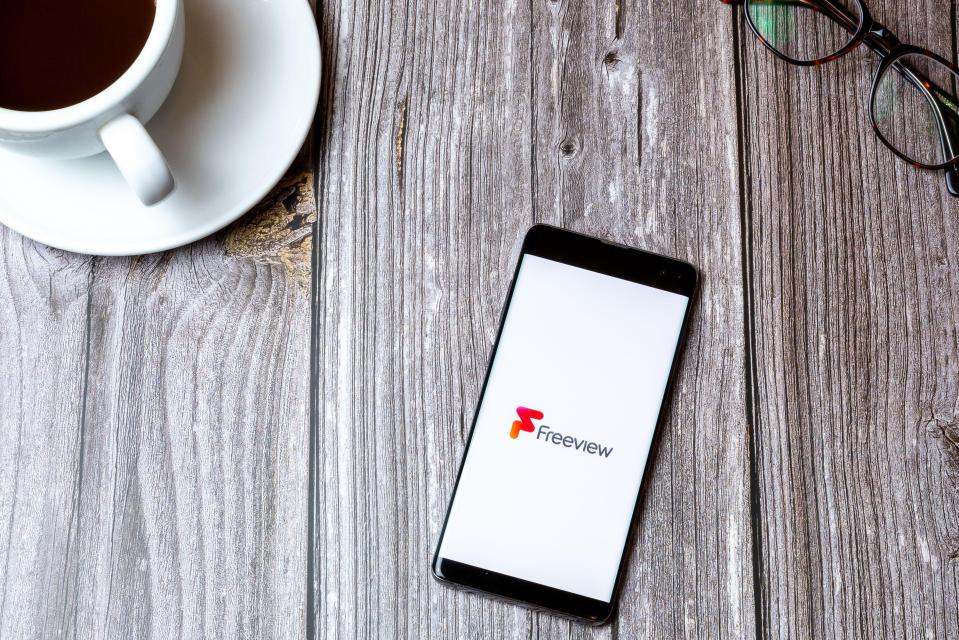 Smartphone displaying the Freeview app on a wooden table next to a cup of coffee and eyeglasses.