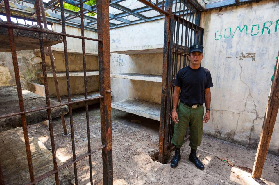 A Panamanian police officer stands in a dilapidated prison cell.
