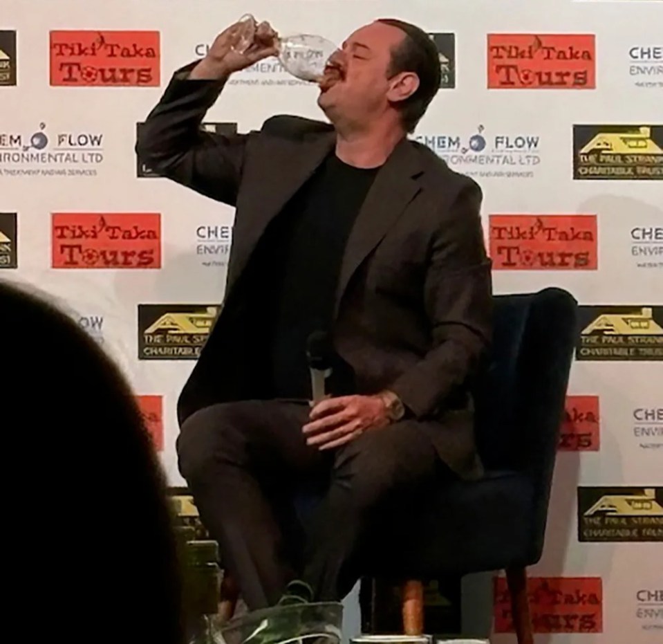 Man in suit drinking wine while seated.