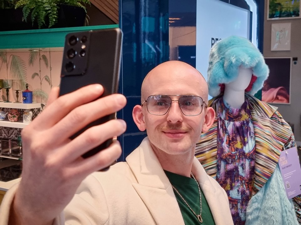 Man taking a selfie with a Samsung Galaxy S21 Ultra 5G phone, showcasing sustainable fashion designs.