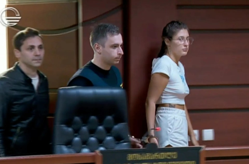 A woman in handcuffs sits in a courtroom.