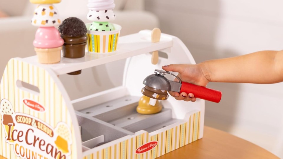 Child using a toy ice cream scoop to serve ice cream from a toy ice cream stand.