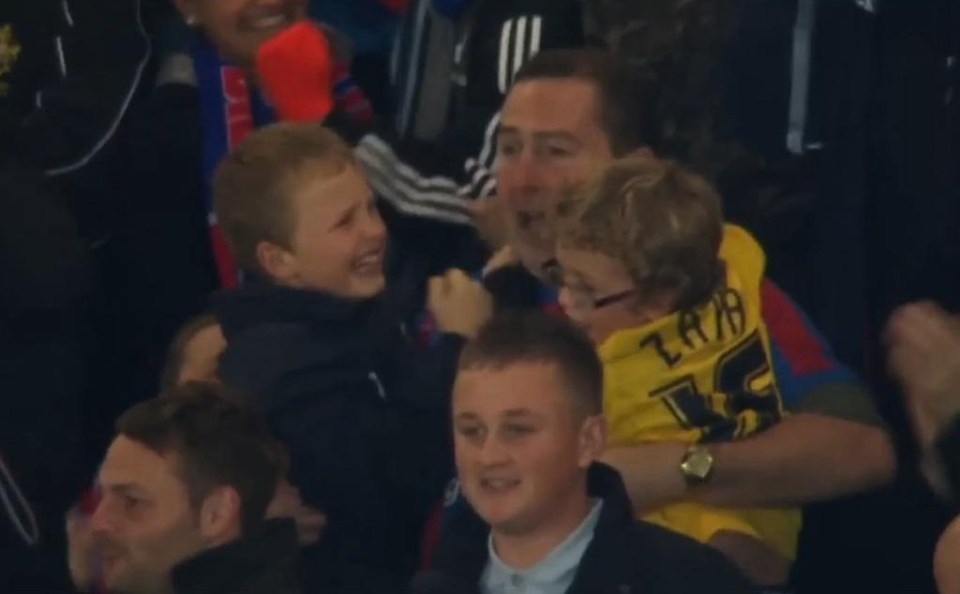 Crowd holding a large banner of a player at a soccer game; below, children and adults in the stands.