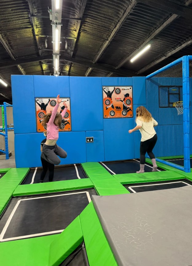 Two girls jumping on trampolines in an indoor trampoline park.