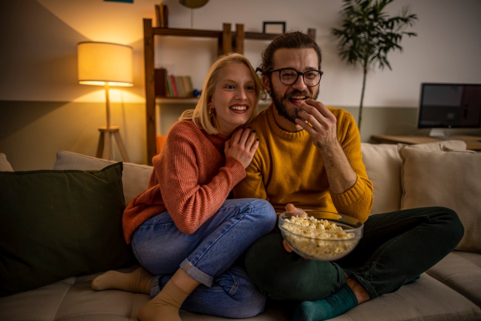 Couple watching TV and eating popcorn on a couch.