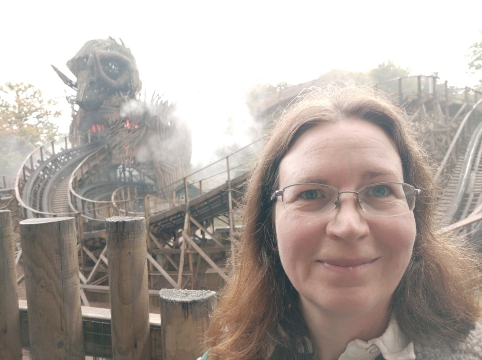 Woman in glasses in front of a wooden rollercoaster.