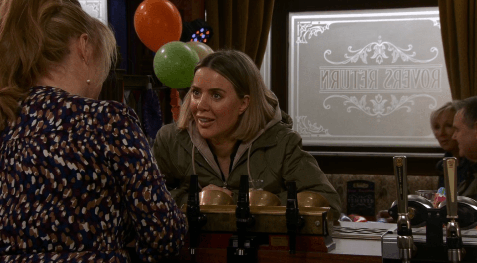 Screenshot of two women talking at a bar with balloons in the background.